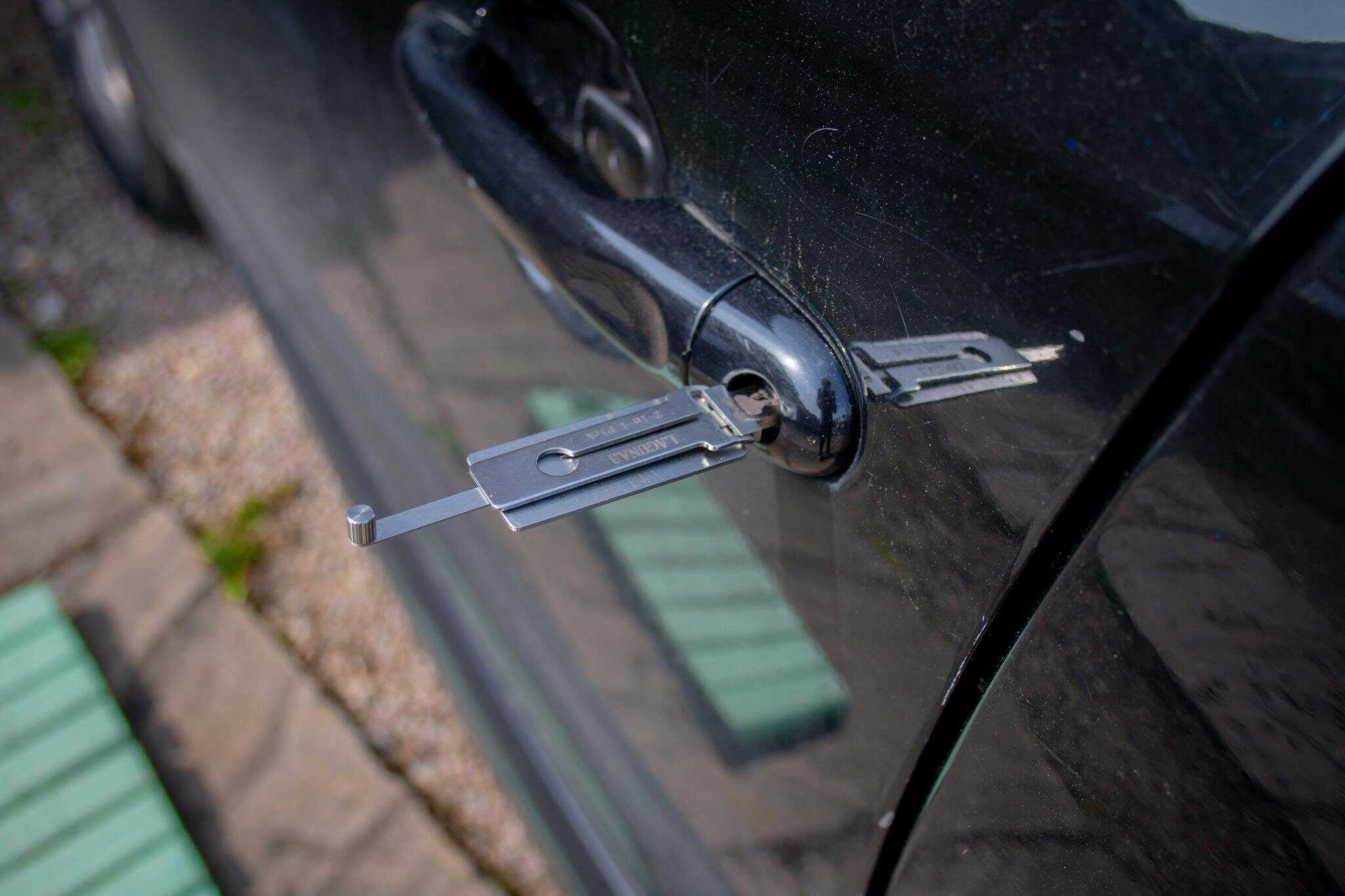 Close-up of a locksmith tool inserted into a car door lock, demonstrating security access.